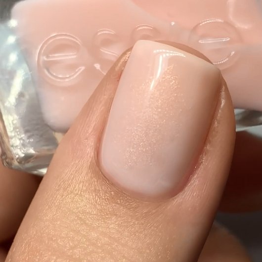 Nail painted with light pink shimmery polish with a bottle of essie nail polish in the background