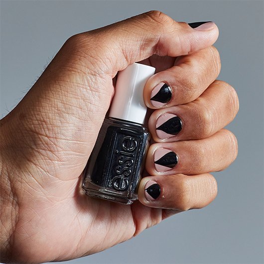close-up of a light skin hand with werewolf nail art holding a bottle of black essie nail polish 
