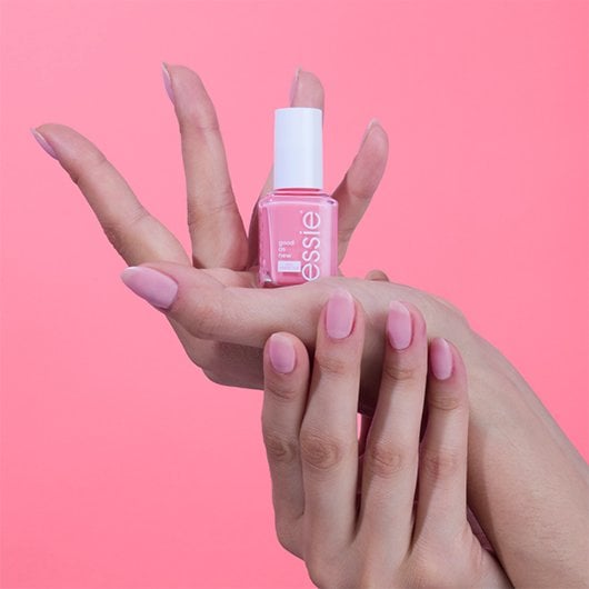 Light skin model wearing pink nail polish and holding a bottle of essie good as new nail perfector