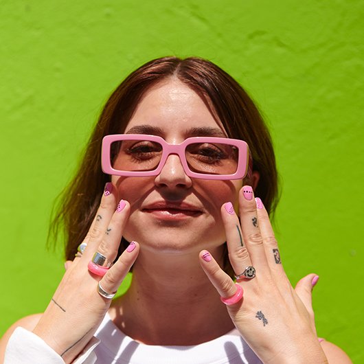 Model with pink sunglasses and pink nails against a bright green background
