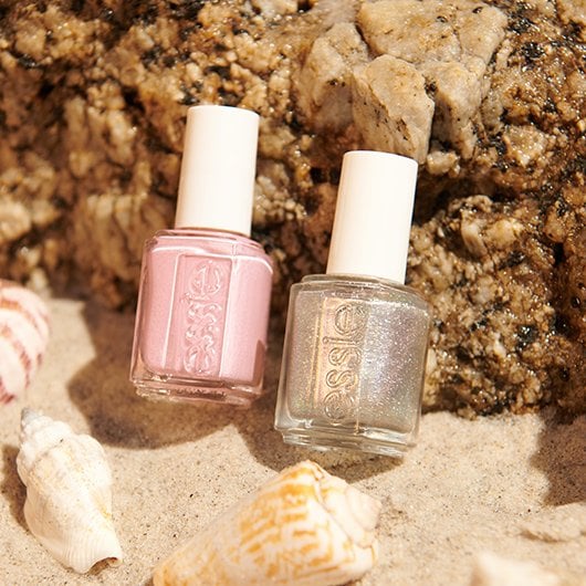 Two bottles of essie nail polish in silver and pink against a sandy beach background