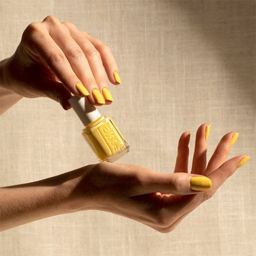 Two model hands with a yellow manicure holding a bottle of yellow essie nail polish