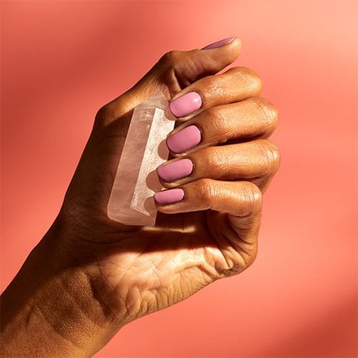 Model's hand with pink manicure holding rose quartz against a pink background