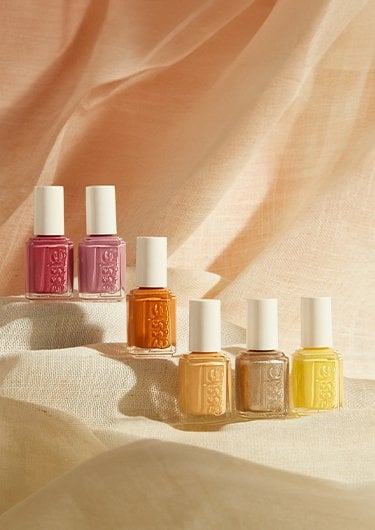 Six bottles with shades of yellow, orange and pink nail polish against a beige linen background