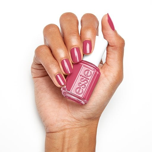 Model with a pink manicure holding a bottle of pink essie nail polish against a white background