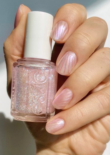 Light skin hand holding pink shimmer nail polish bottle wearing seashell pearl nail design