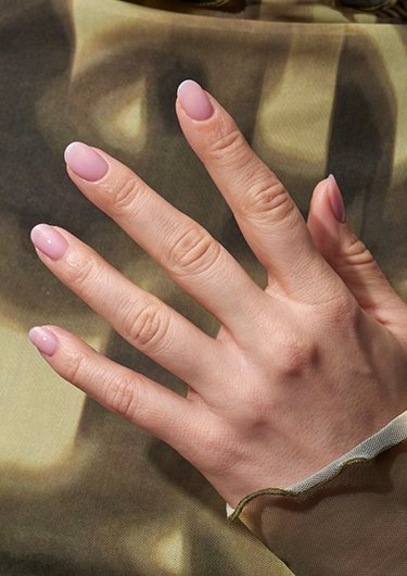 Hand with lip gloss nails against a light and dark green background
