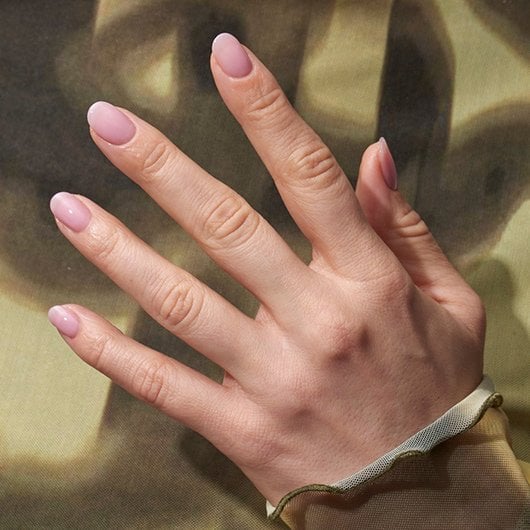 Hand with lip gloss nails against a light and dark green background