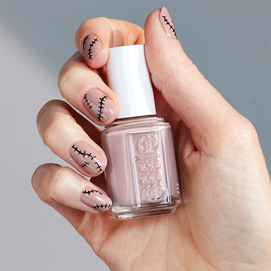 light skin hand with stitchy nail art holding a bottle of neutral essie nail polish 