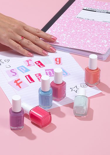 Light skin hand on note "spring fling" with a pink notebook and bottles of polish on a pink desk
