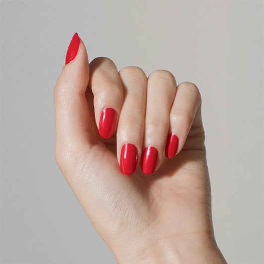 Light skin hand with fingers folded over wearing apple red just take a bite essie polish